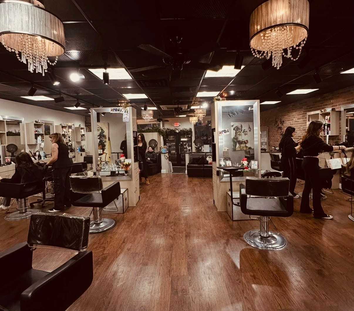 Modern hair salon interior with hairstylists and clients; chandeliers and mirrors adorn the space.